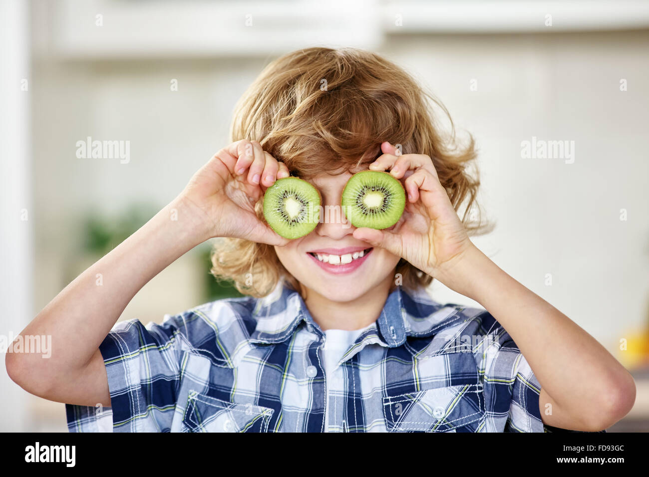 Ragazzo divertendosi con kiwi e tenendo il frutto di fronte ai suoi occhi Foto Stock