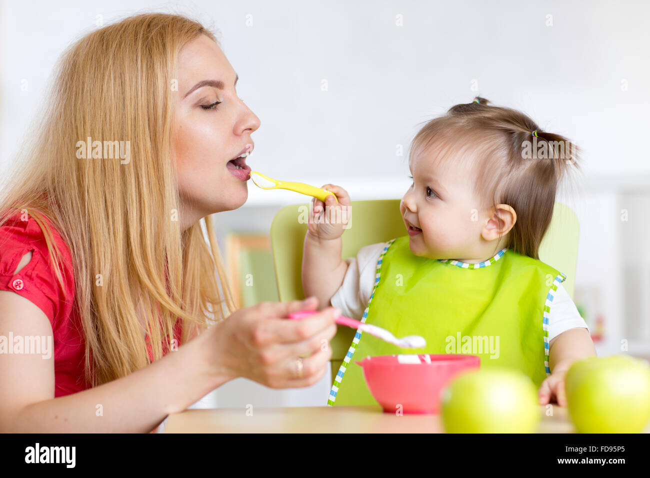 Bambina e madre con bambino cibo alimentazione di ogni altra seduta a tavola in vivaio Foto Stock