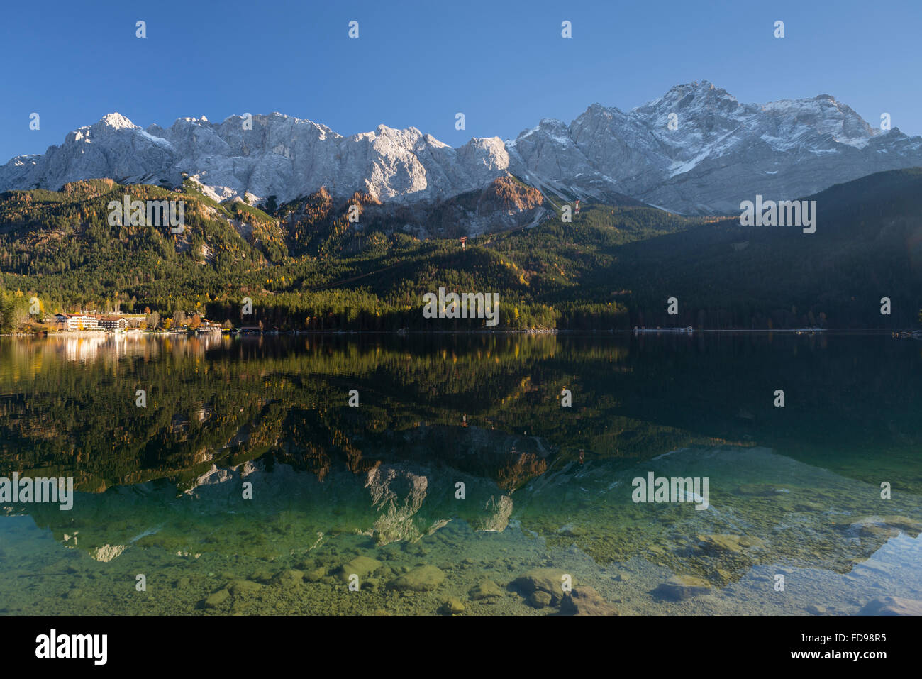 Lago Eibsee prima di Wetterstein gamma di montagna e il monte Zugspitze con autunno le foreste e gli alberi in un caldo pomeriggio di sole Foto Stock