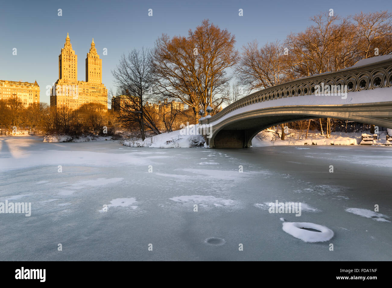 Il freddo Central Park inverno alba sul lago ghiacciato con il ponte di prua e Upper West Side di edifici. Manhattan, New York City Foto Stock