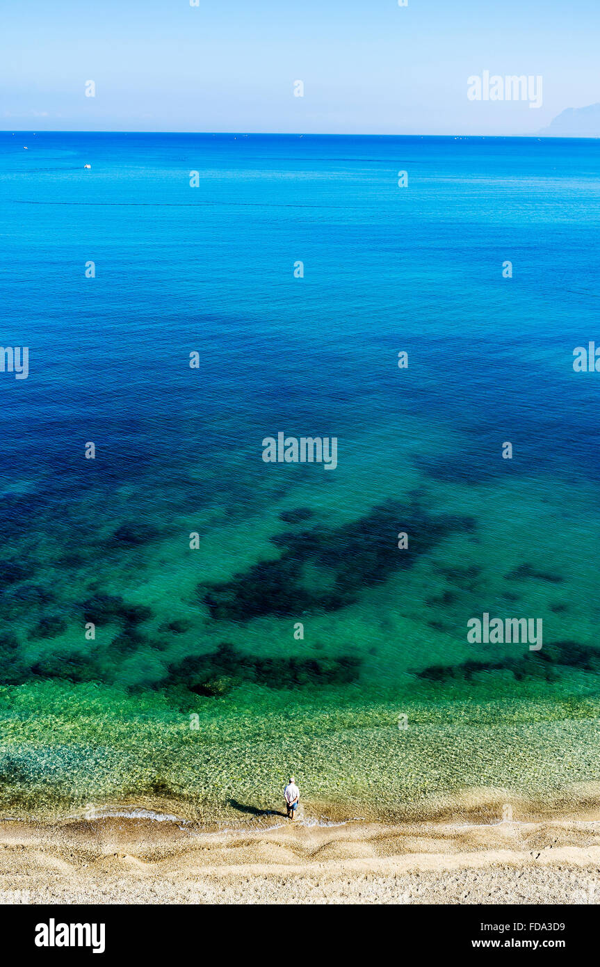 Uomo in piedi da solo su una spiaggia a Waters Edge, Sicilia, Italia Foto Stock