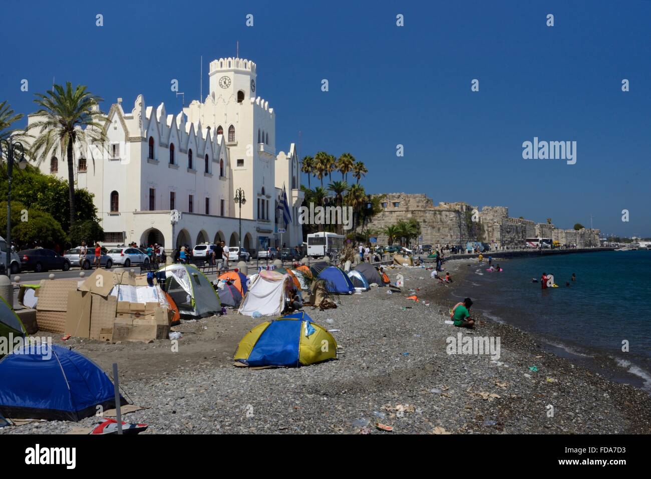 I migranti camping sulla spiaggia e nuotare nel mare nella cittadina di Kos e di fronte alla stazione di polizia, Kos, Grecia. Foto Stock