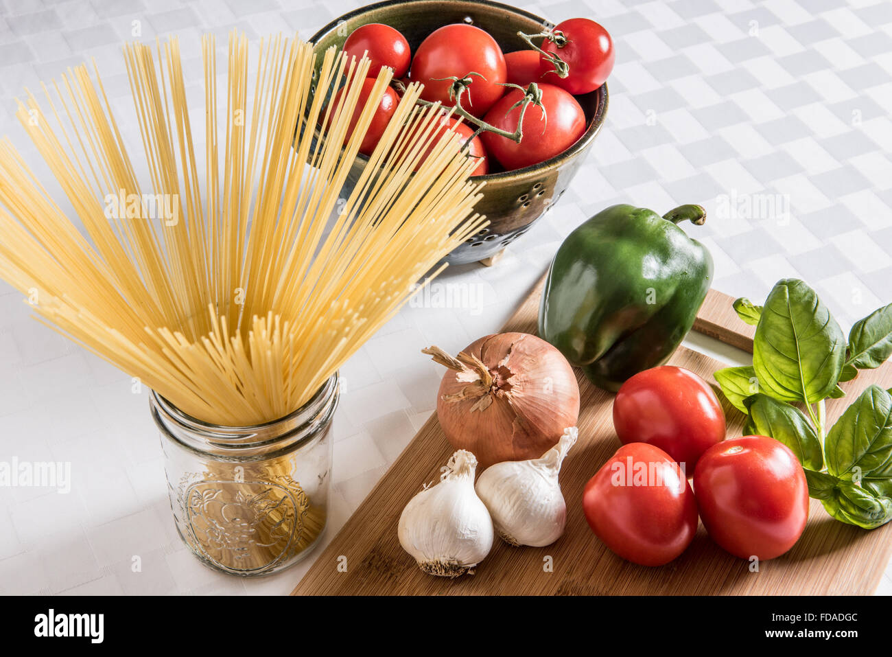 Ingredienti italiani freschi esposti su un tagliere di legno con pasta di capelli d'angelo essiccata e un colino di ceramica di pomodori maturi su un panno bianco. Foto Stock