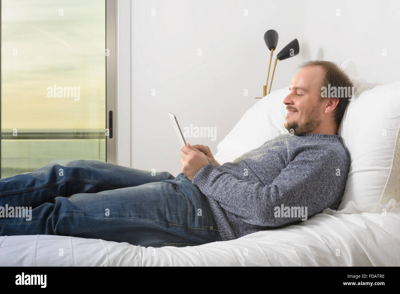 Uomo disteso bed sorridente tablet tramonto Foto Stock