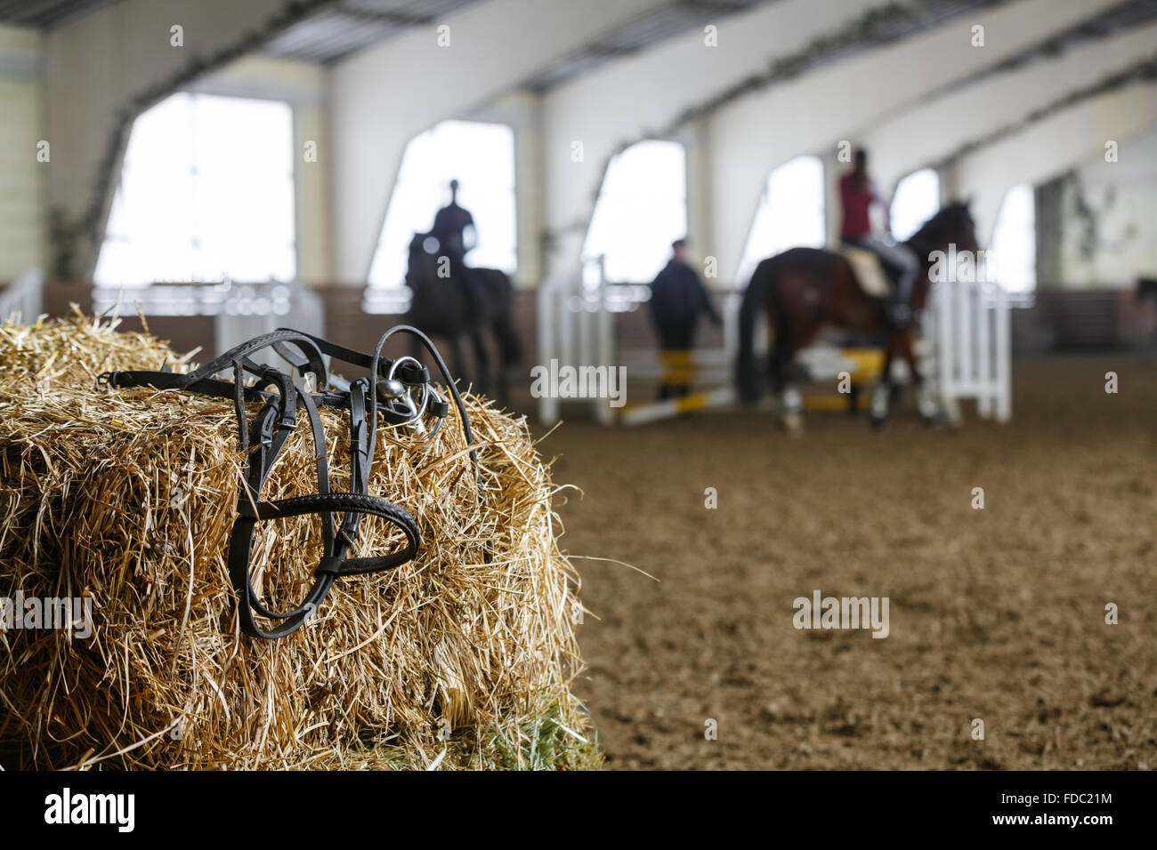 Attrezzatura per cavalli giacente su un fresco di mattoni di fieno su un maneggio. Blured irriconoscibile cavalieri su uno sfondo Foto Stock