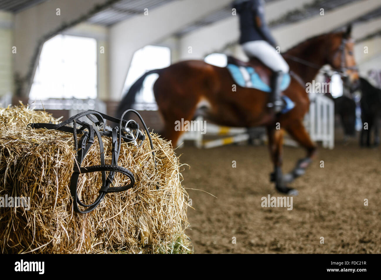 Attrezzatura per cavalli giacente su un fresco di mattoni di fieno su un maneggio. Blured irriconoscibile cavalieri su uno sfondo Foto Stock