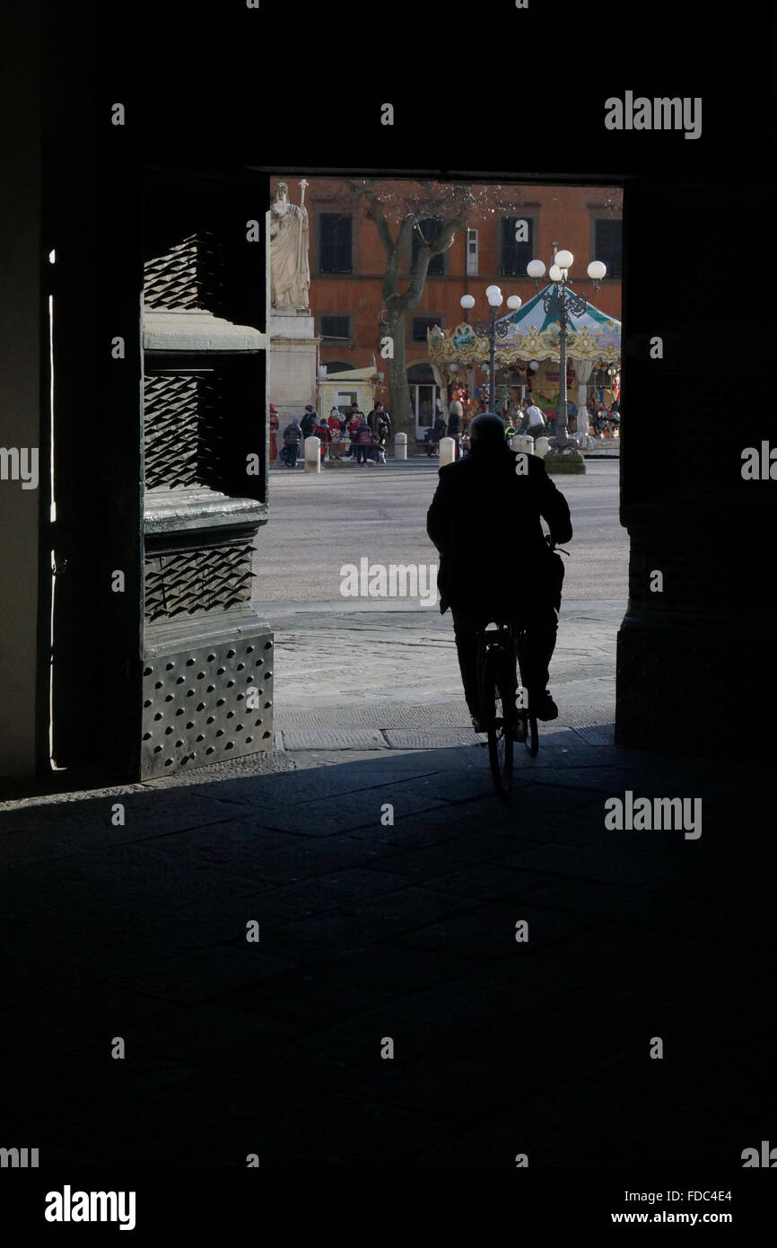 Ciclista passeggiate attraverso una grande porta a una plaza a Lucca, Italia Foto Stock