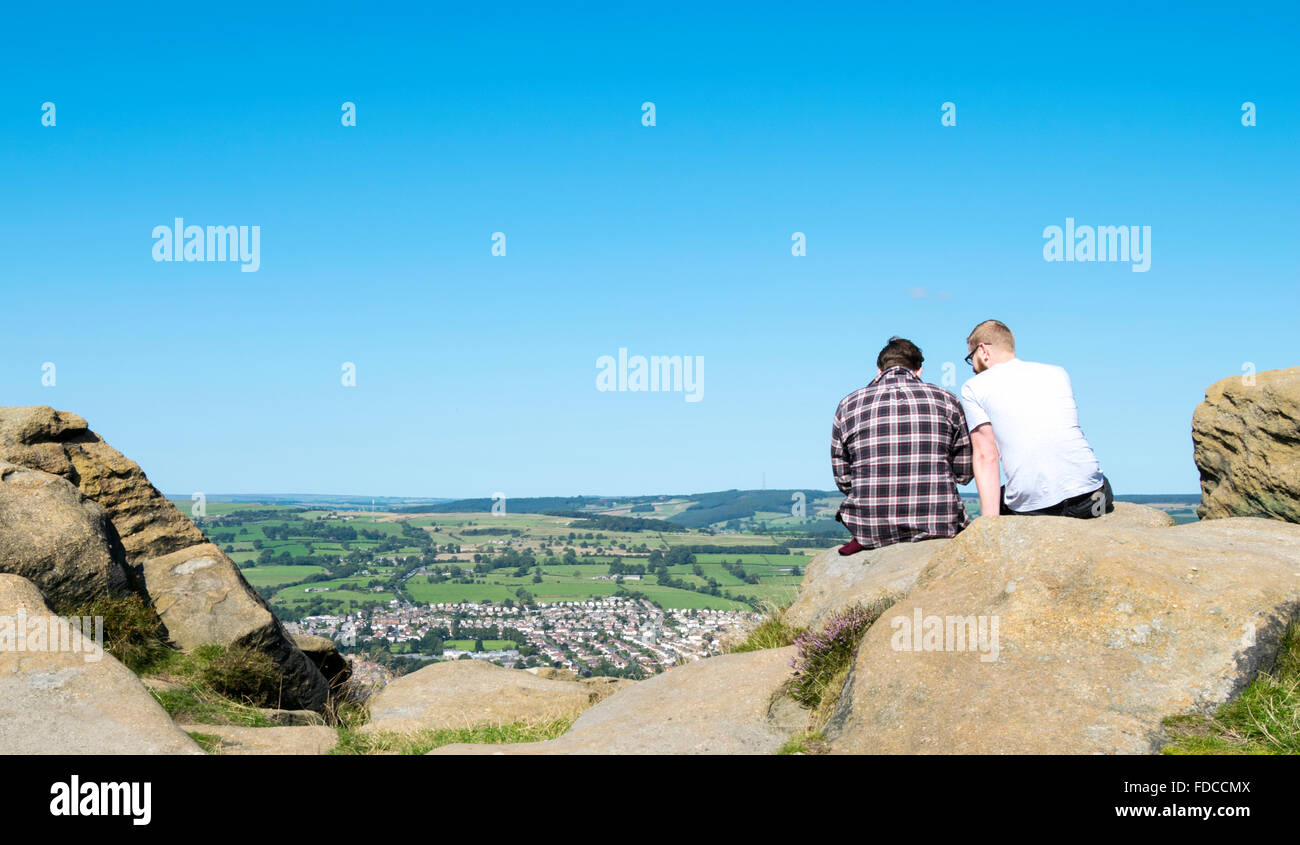Due persone sedute su una roccia di arenaria che si affaccia a Otley Chevin Forest Park, West Yorkshire, Regno Unito. Foto Stock