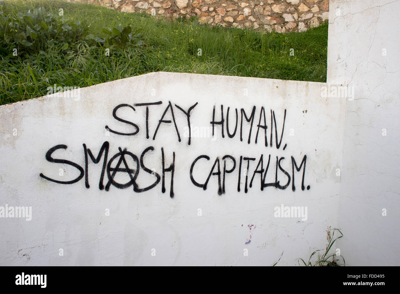 Restiamo umani smash capitalismo verniciato a spruzzo su un muro bianco Foto Stock