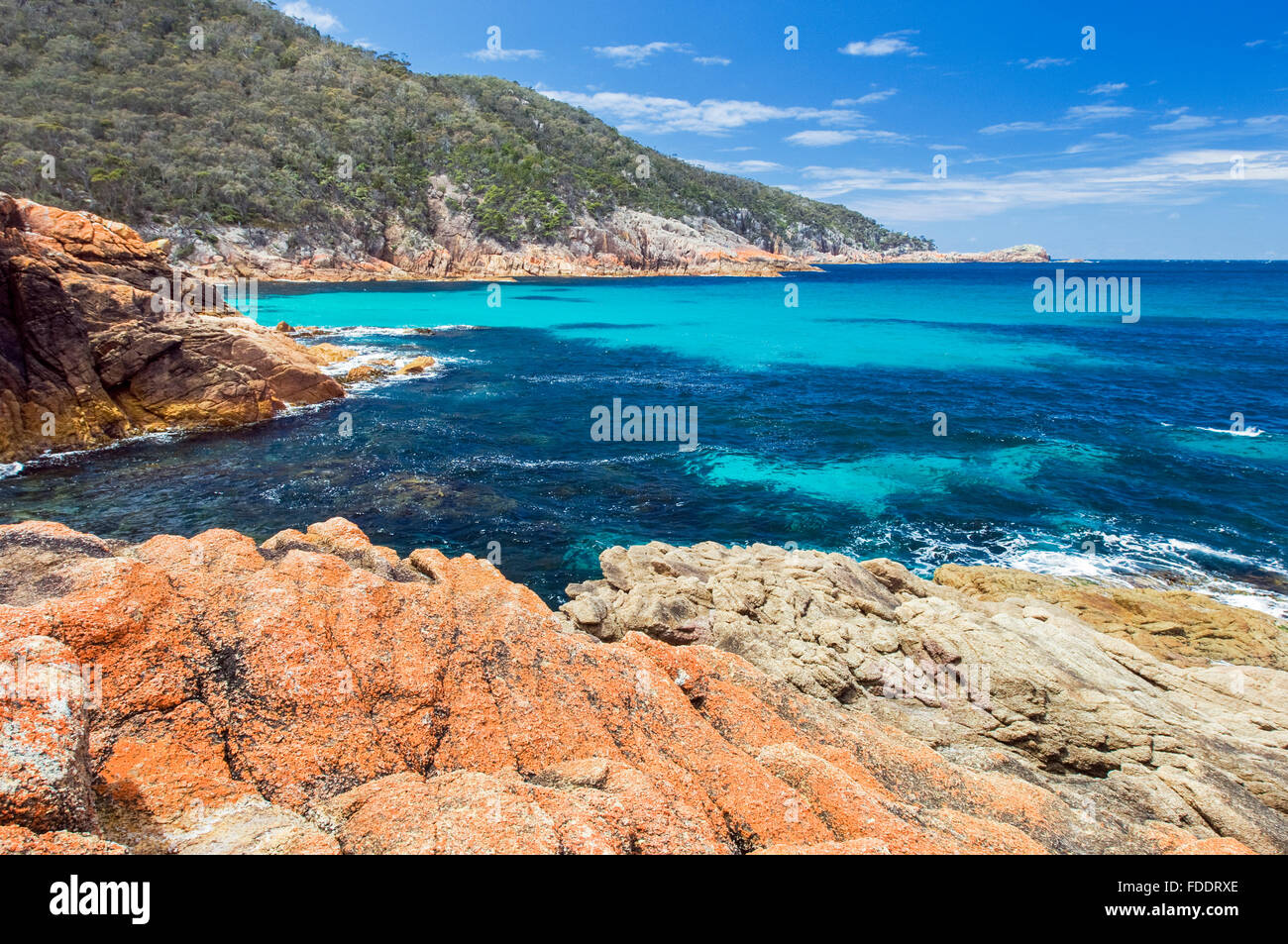 Assonnato Bay, il Freycinet, Tasmania, Australia con cielo blu, acqua chiara e lichene arancione rocce coperte Foto Stock