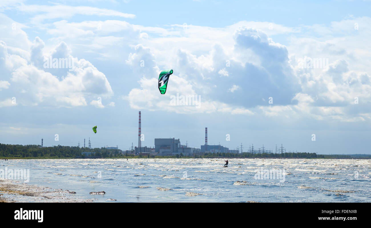 Sosnovy Bor, Russia - Luglio 19, 2015: Kitesurfisti cavalcare le onde del golfo di Finlandia con la centrale nucleare di Leningrado Impianto di alimentazione Foto Stock