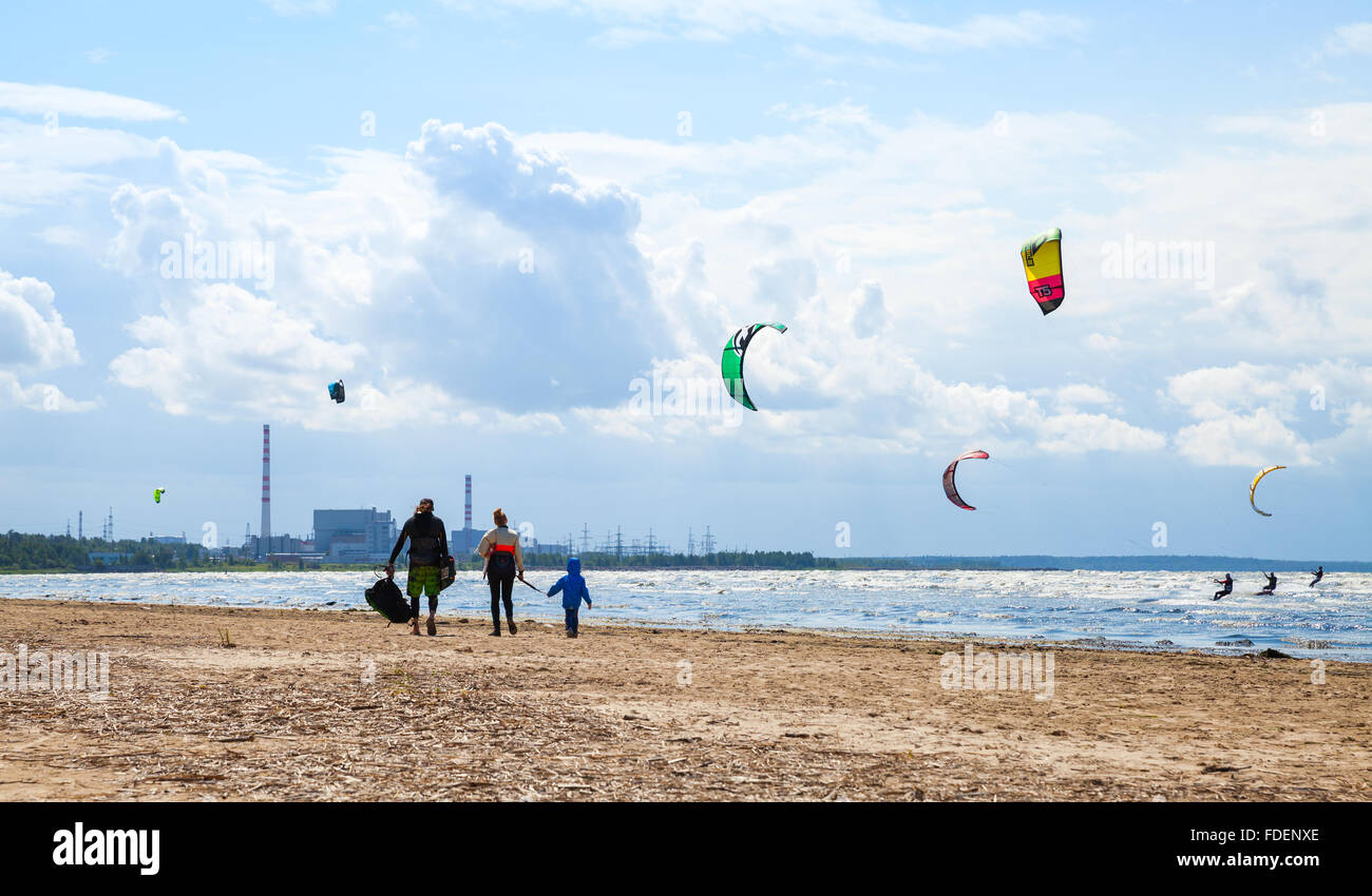 Sosnovy Bor, Russia - Luglio 19, 2015: Famiglia di camminare sulla spiaggia. Kitesurfisti cavalcare le onde del golfo di Finlandia Foto Stock