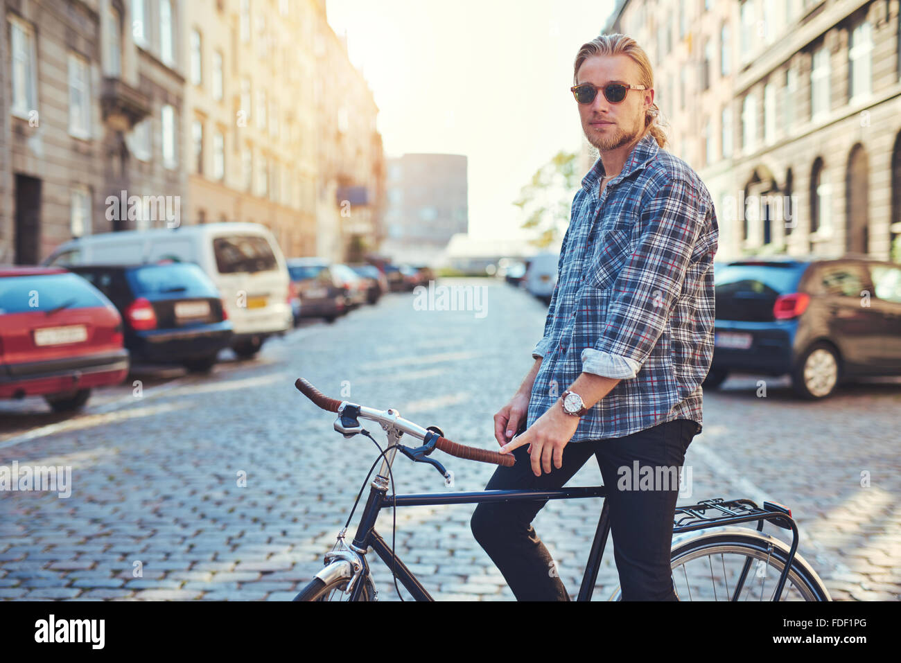 Lo stile di vita della città, ritratto di uomo con capelli biondi e occhiali da sole seduto sulla sua moto Foto Stock