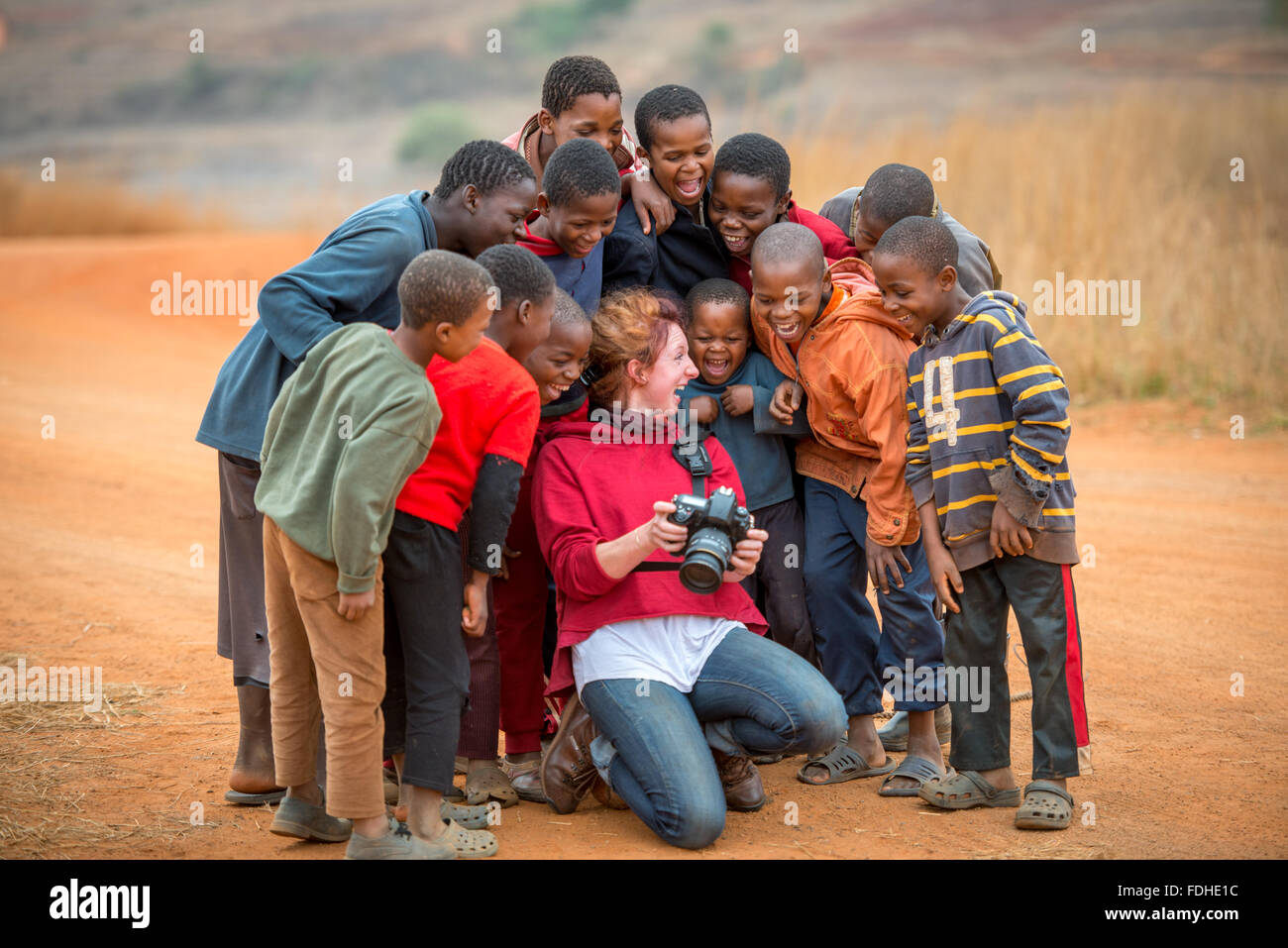 Giovani ragazzi africani in piedi intorno a una ragazza americana guardando la sua fotocamera nella regione Hhohho dello Swaziland, Africa. Foto Stock