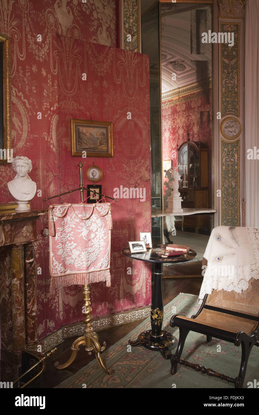 Vista parziale del caminetto e un incendio a schermo e lo specchio in Boudoir ad Arlington corte, Devon. La camera era destinata ad essere una donna di ritirarsi e ha in rosa e oro parete di seta-impiccagioni. Foto Stock