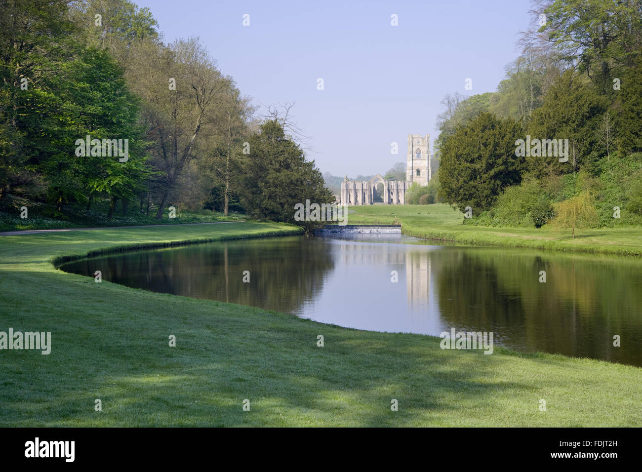 Una vista sopra la Mezza Luna stagno e weir di Studley Royal acqua giardino verso Fountains Abbey, North Yorkshire. Fountains Abbey, una comunità cistercense di monaci fondata nel XII secolo, costituisce un pittoresco sfondo per i giardini d'acqua creato da J Foto Stock