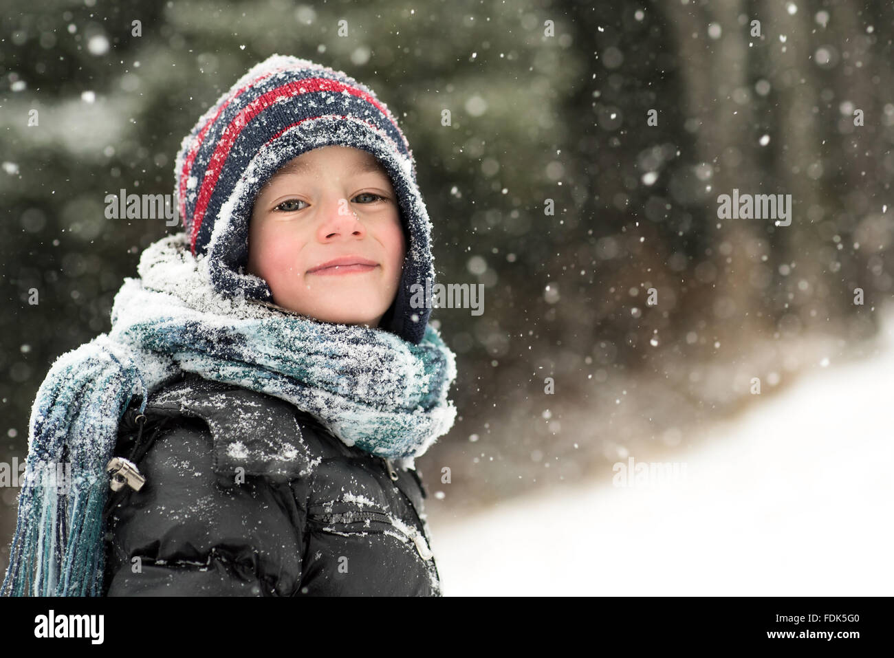 Ragazzo sorridente in piedi nella foresta nella neve Foto Stock