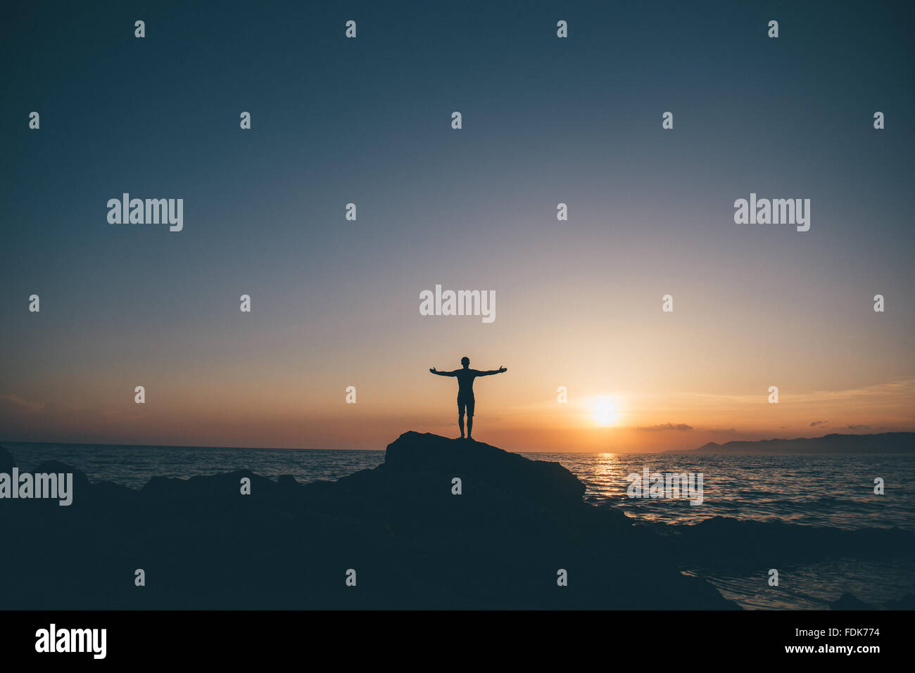 Silhouette di un uomo in piedi sulle rocce con le braccia aperte Foto Stock