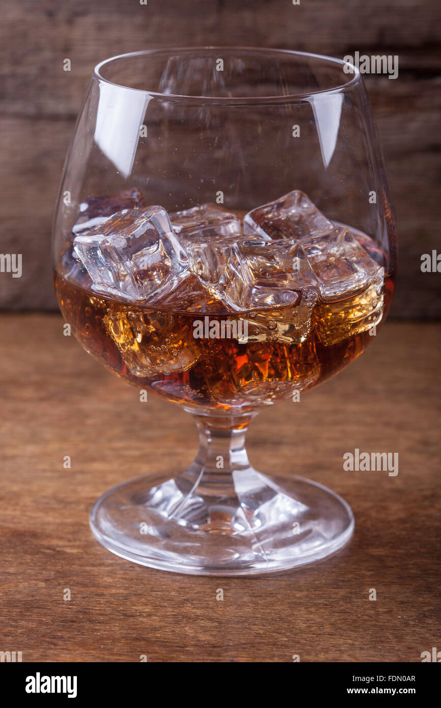 Cognac in un bicchiere con ghiaccio su sfondo di legno closeup Foto Stock
