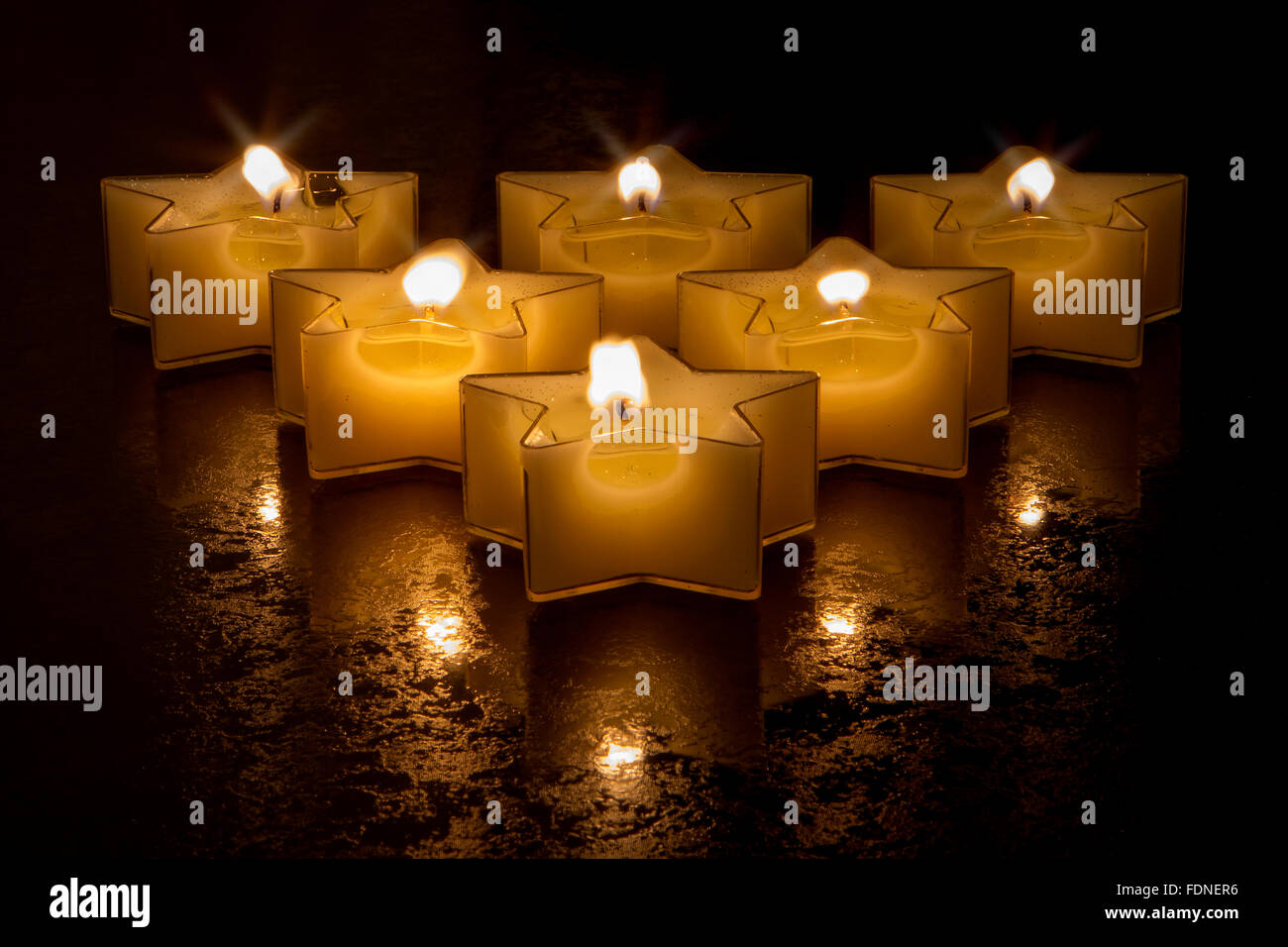 Sei a forma di stella candele in una formazione triangolare incandescente su una superficie strutturata la superficie nera Foto Stock