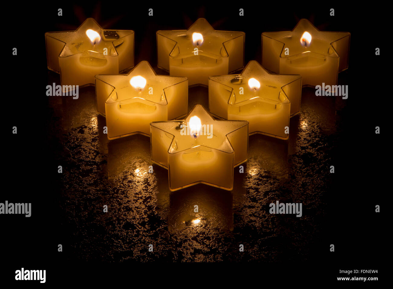 Sei a forma di stella candele in una formazione triangolare incandescente su una superficie strutturata la superficie nera Foto Stock