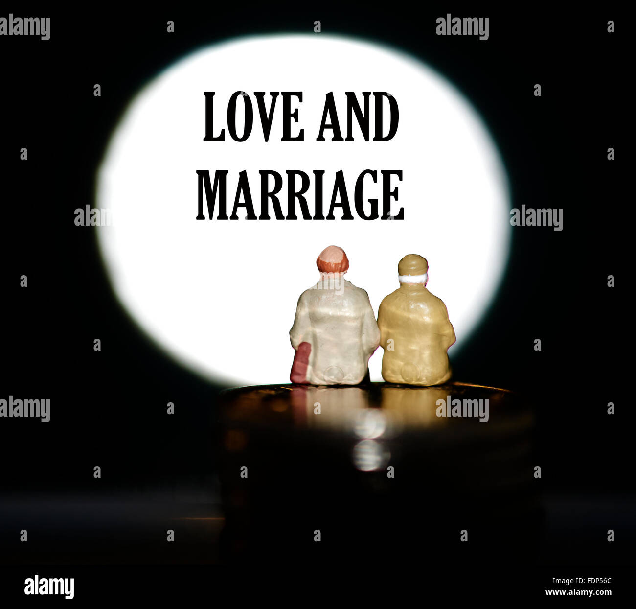 Statuetta in miniatura pensionati seduti sulle monete di fronte un faretto che mostra le parole di amore e di concetto di matrimonio Foto Stock