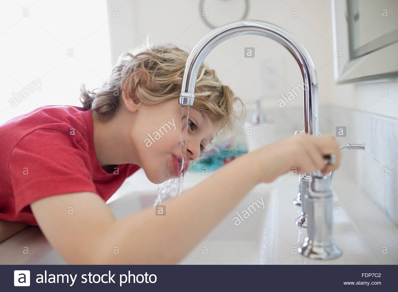 Ragazzo di bere acqua dal rubinetto da bagno Foto Stock