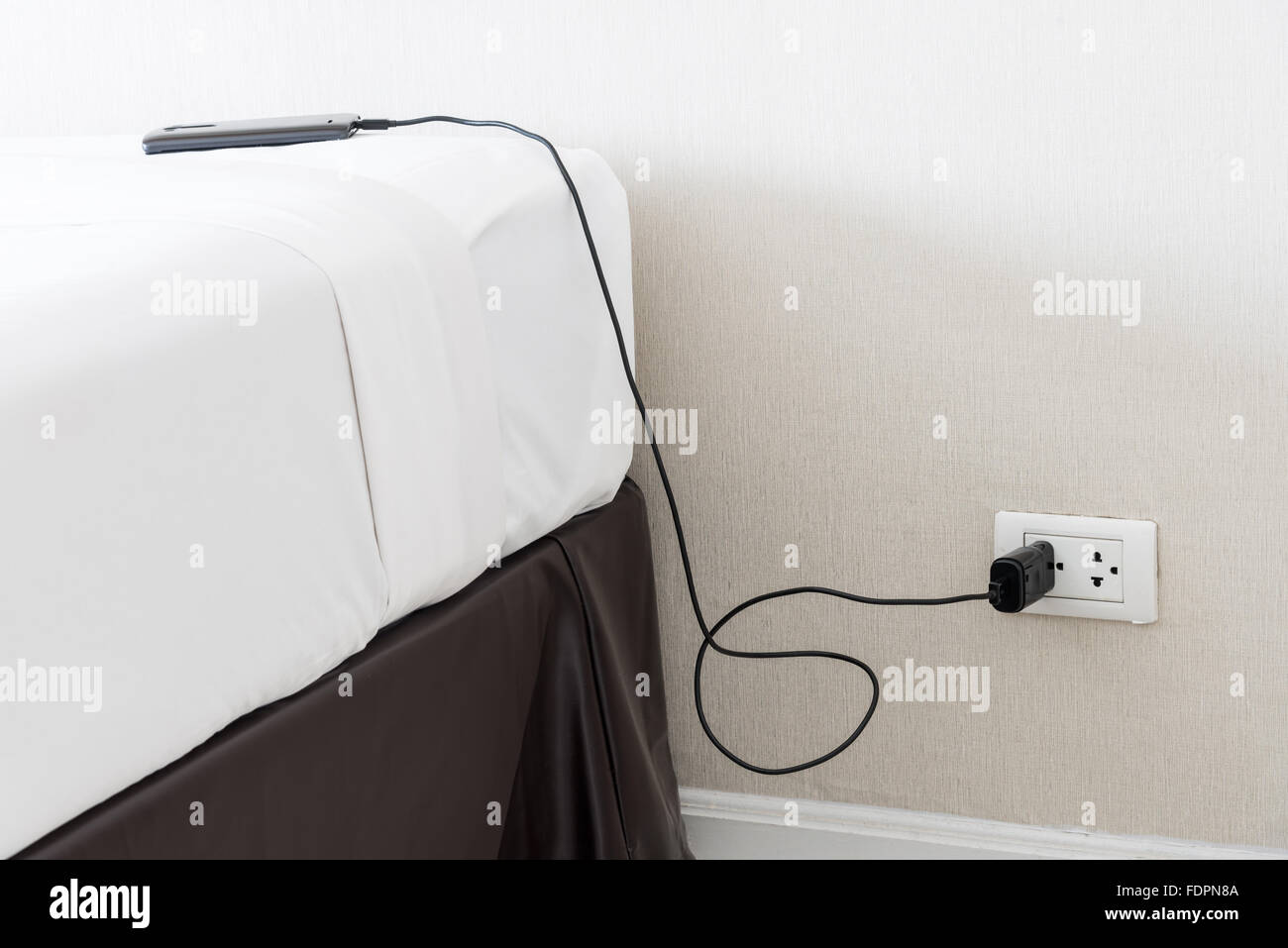 Il telefono cellulare caricabatteria con presa a muro in camera da letto. Foto Stock