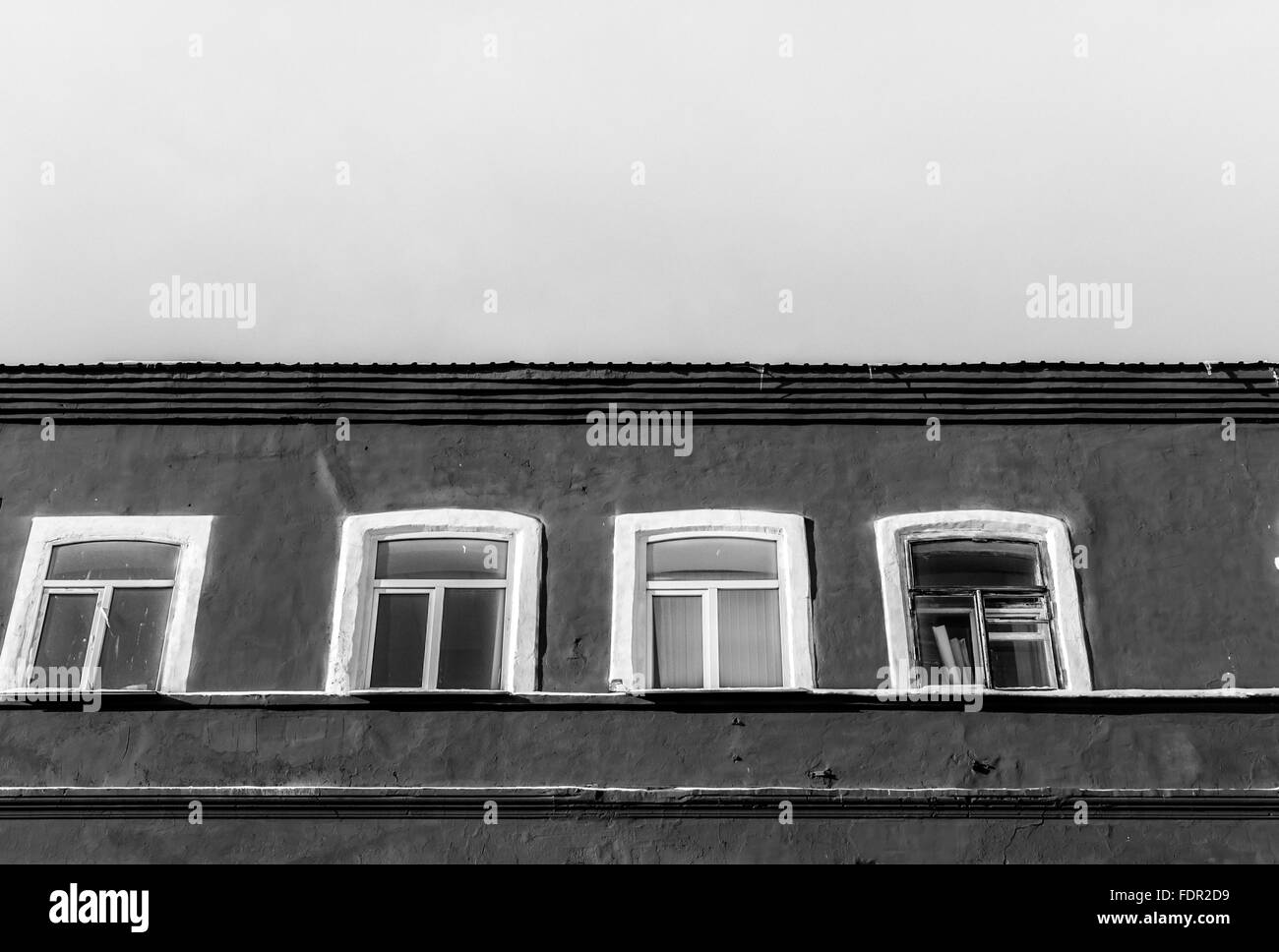 Luminose monocromatiche e posteriore verniciato bianco edificio di età con quattro finestre bianche insieme contro un chiaro scuro Cielo di estate. Architettura Foto Stock