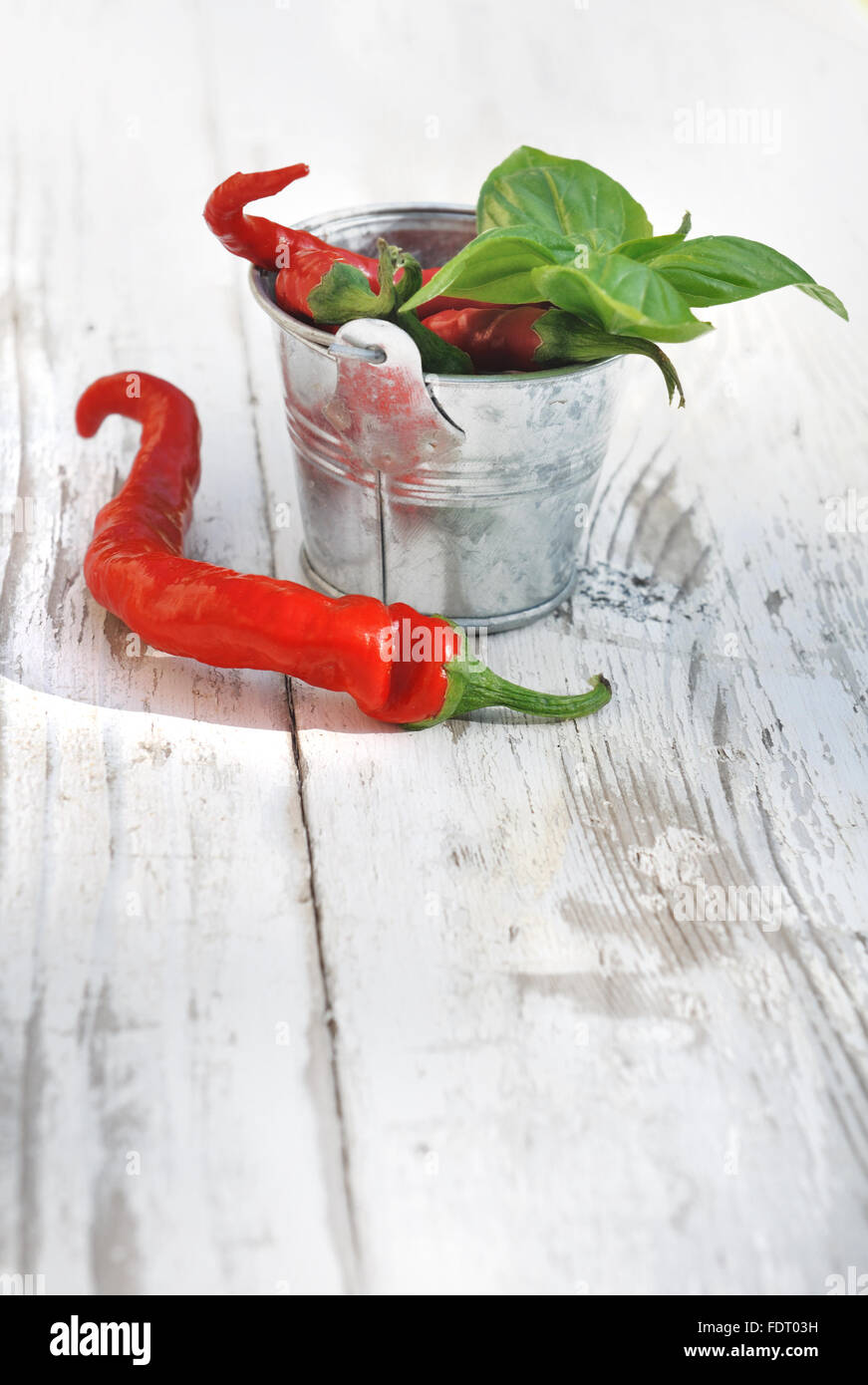 Peperoni rossi e basilico su un piccolo vaso sul tavolo bianco Foto Stock