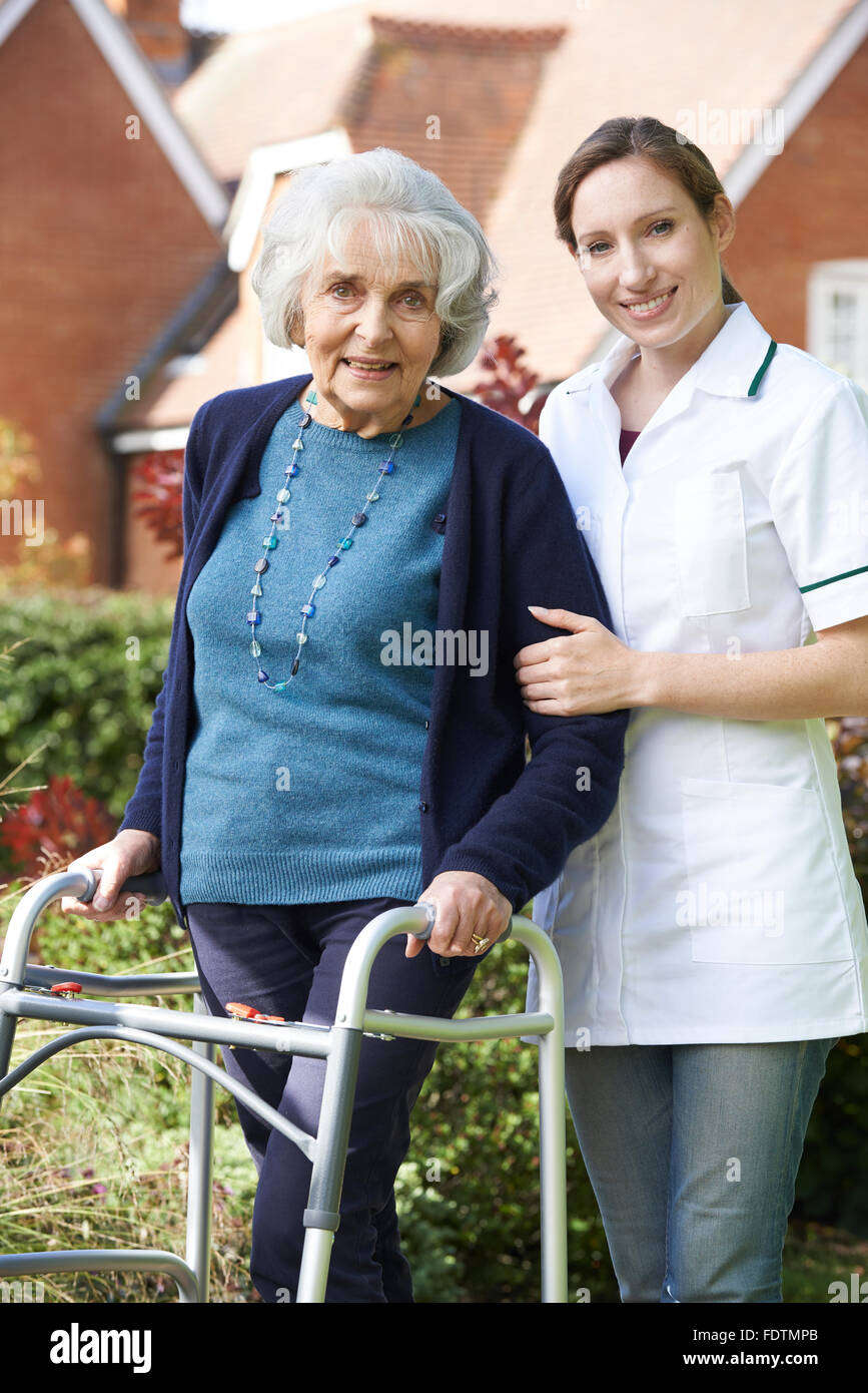 Accompagnatore aiutando Senior donna a camminare nel giardino con telaio a piedi Foto Stock