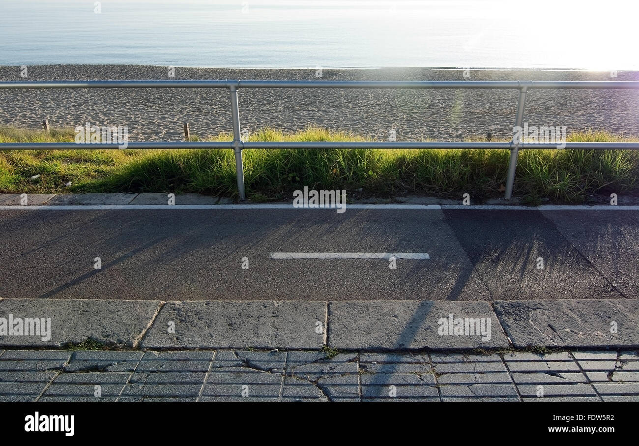 Erba e sabbia lungo il mare ciclismo pista di calcestruzzo con recinto e sunshine lungo il Mediterraneo in una giornata di sole a dicembre Foto Stock