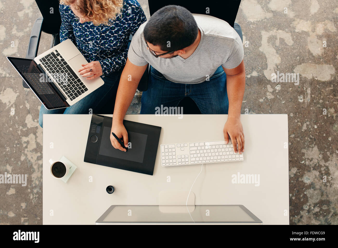 Due giovani facendo graphic design lavoro. Uomo al lavoro su tavoletta grafica e computer mentre donna utilizzando laptop. Sia la seduta t Foto Stock