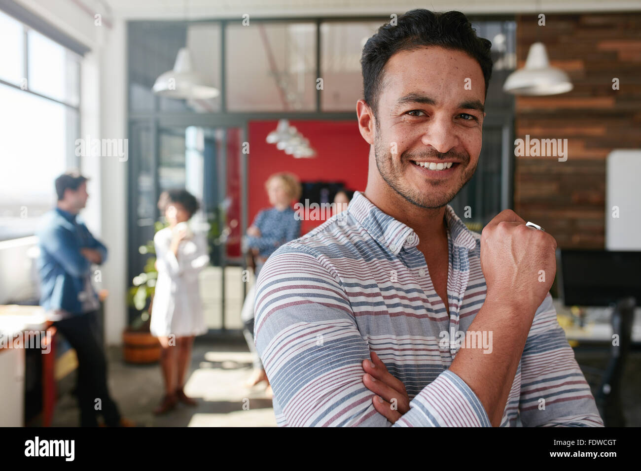 Ritratto di smart creative professional guardando la fotocamera e sorridente. Felice uomo caucasico in piedi in ufficio con i colleghi dis Foto Stock