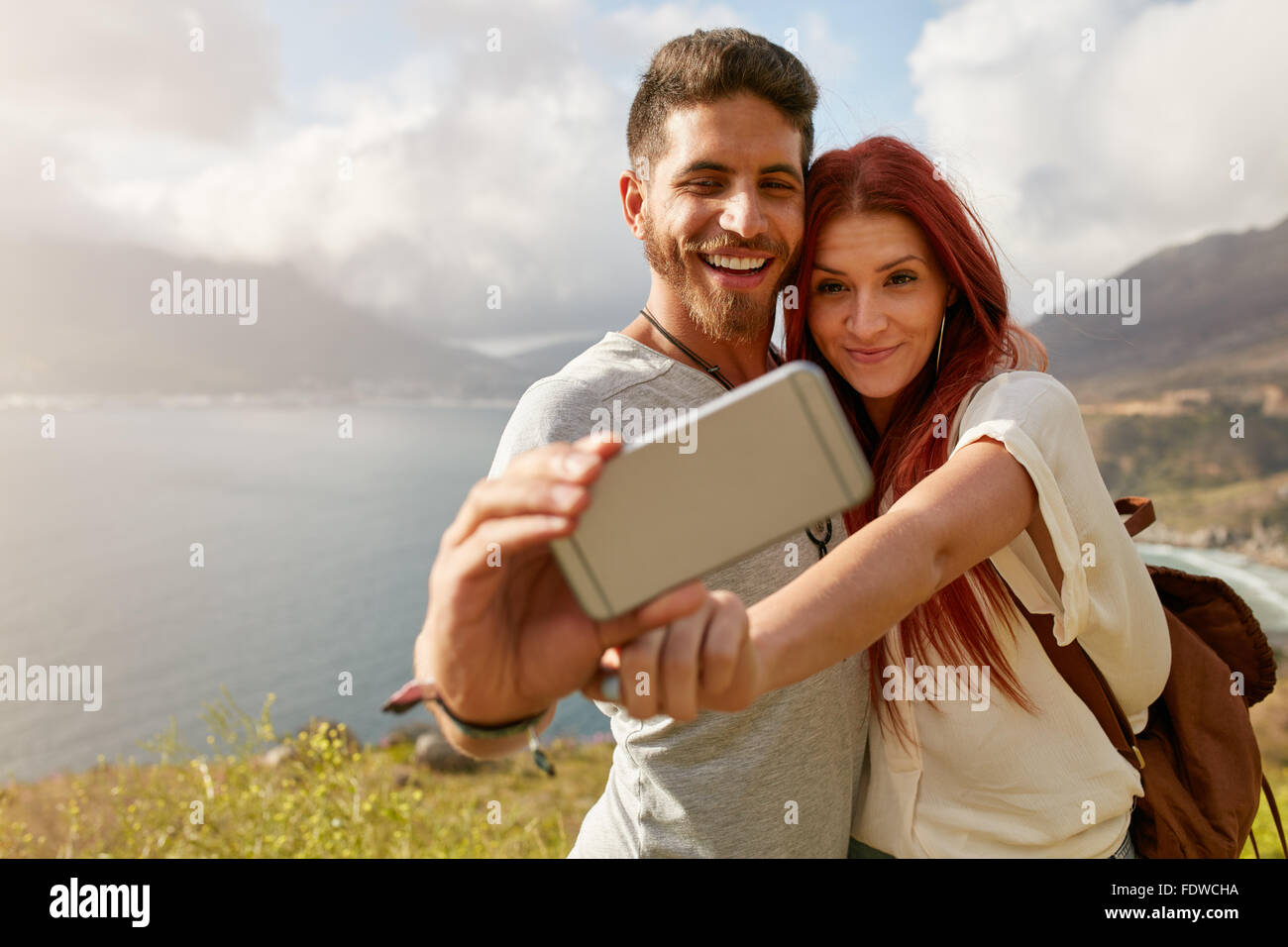Coppia giovane escursionismo tenendo selfie con smart phone. Felice giovane uomo e donna prendendo autoritratto con paesaggio di montagna nel retro Foto Stock