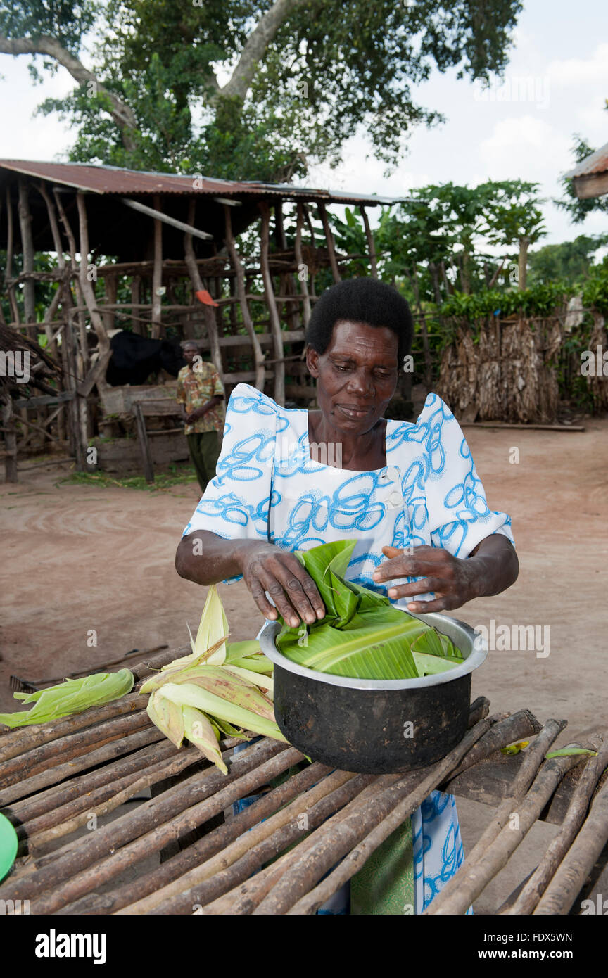 Signora ugandese preparare un pasto in una padella utilizzando il mais e foglie di banano. Uganda. Foto Stock