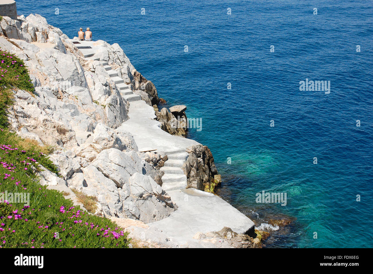 Spiaggia rocciosa con scale e prendere il sole matura in Hydra, Grecia Foto Stock