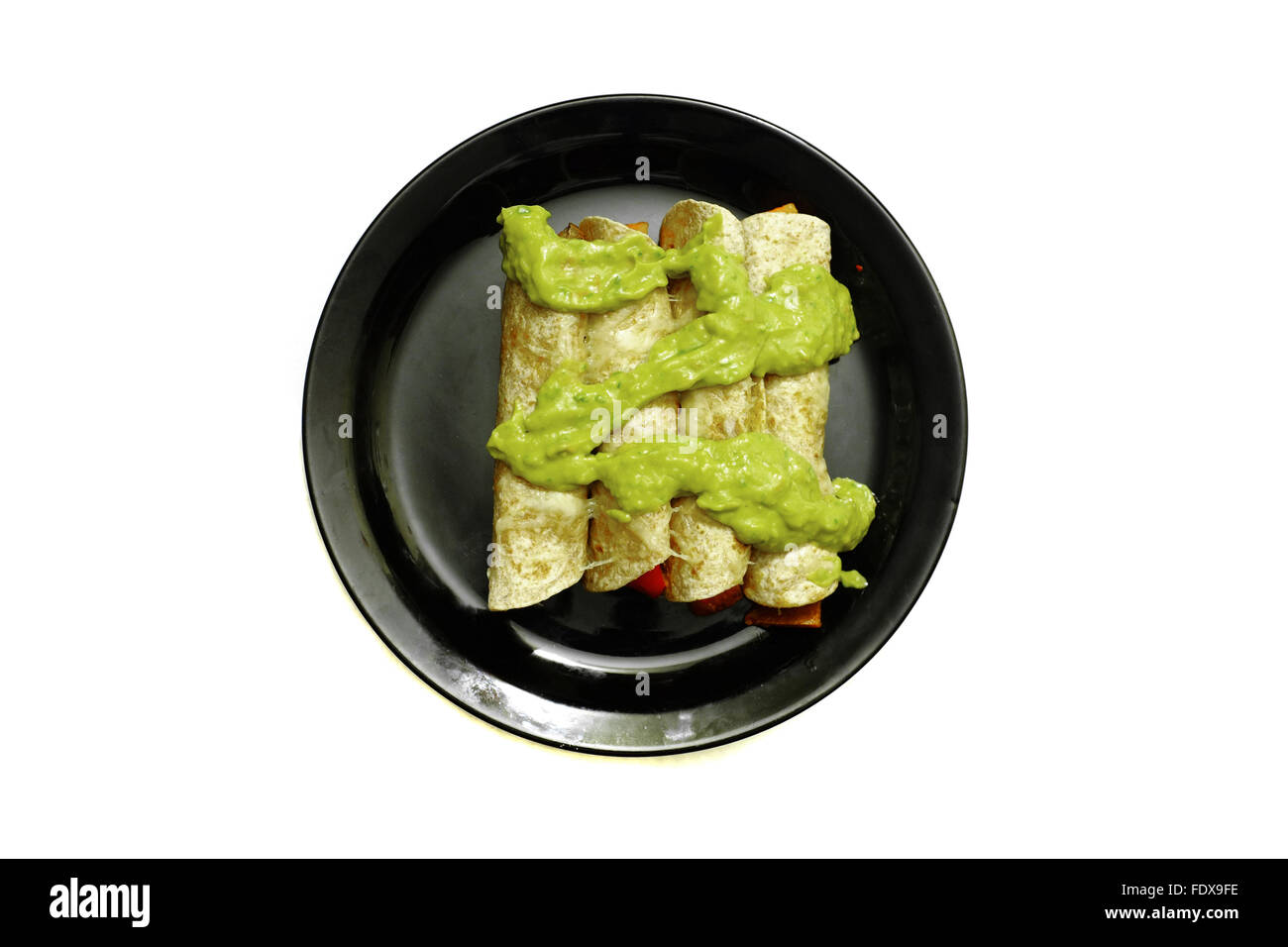 Burrito cotto ricoperto in salsa guacamole su una piastra nera fotografati contro uno sfondo bianco Foto Stock