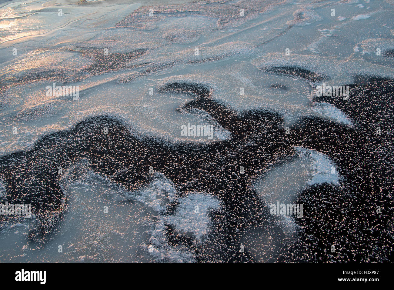 Macchie nere di ghiaccio sul lago miscelati con alcuni fiocchi di neve. Foto Stock
