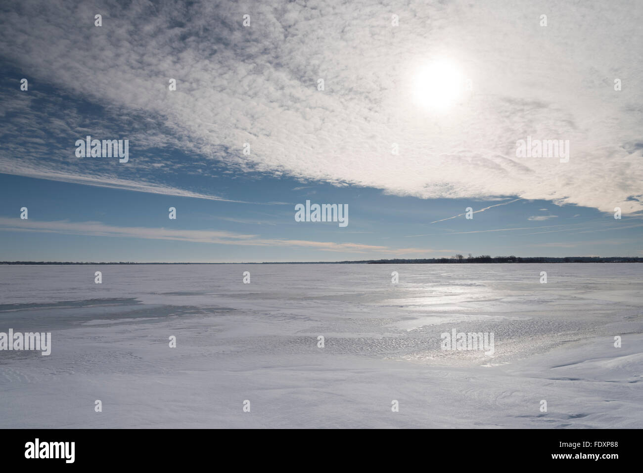 L'abbagliante luce del sole invernale è parzialmente oscurata da un sottile strato di nubi, e riflessa dalla neve e dal ghiaccio che ricopre un lago. Foto Stock