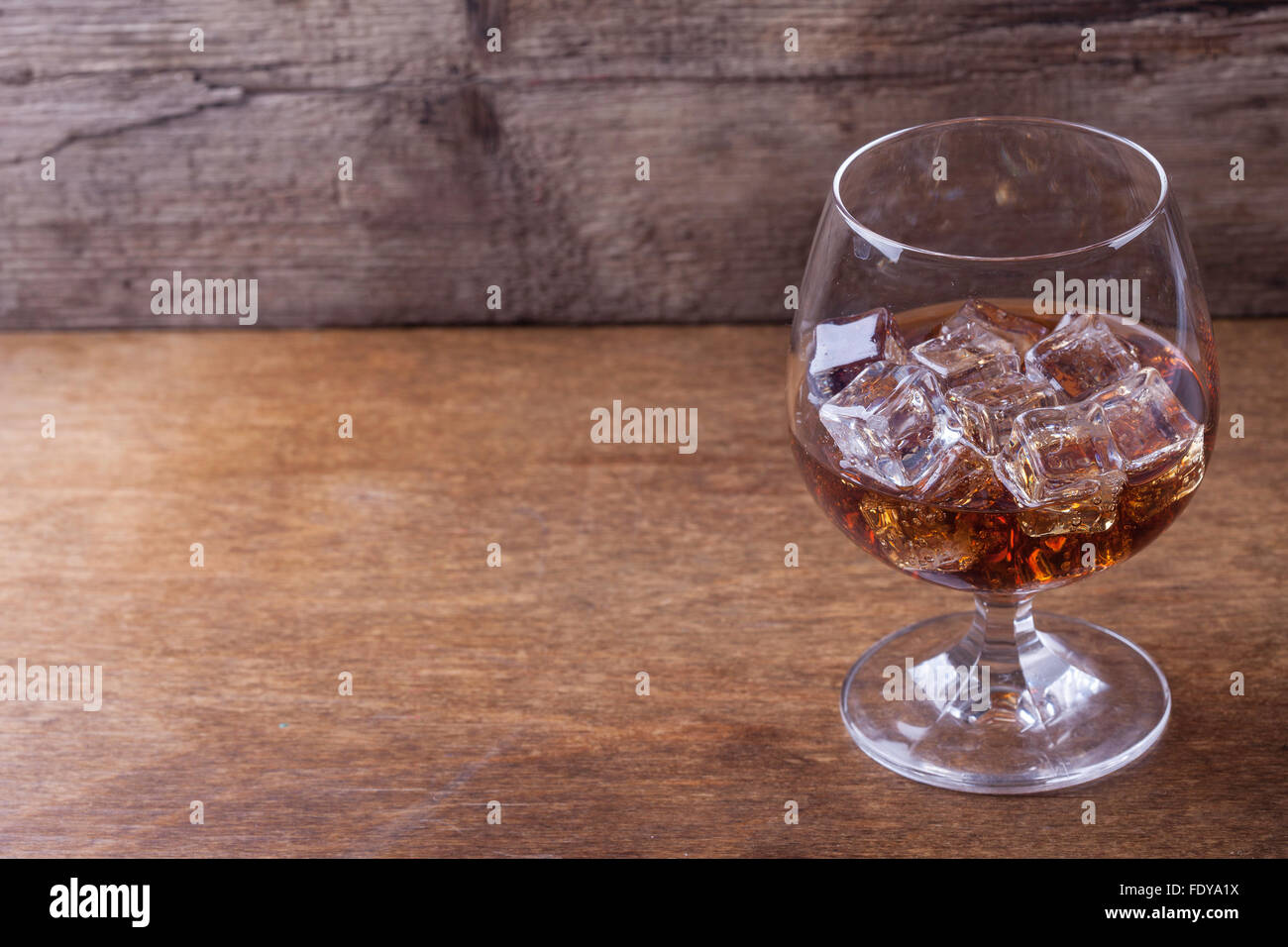 Cognac in un bicchiere con ghiaccio su sfondo di legno closeup Foto Stock