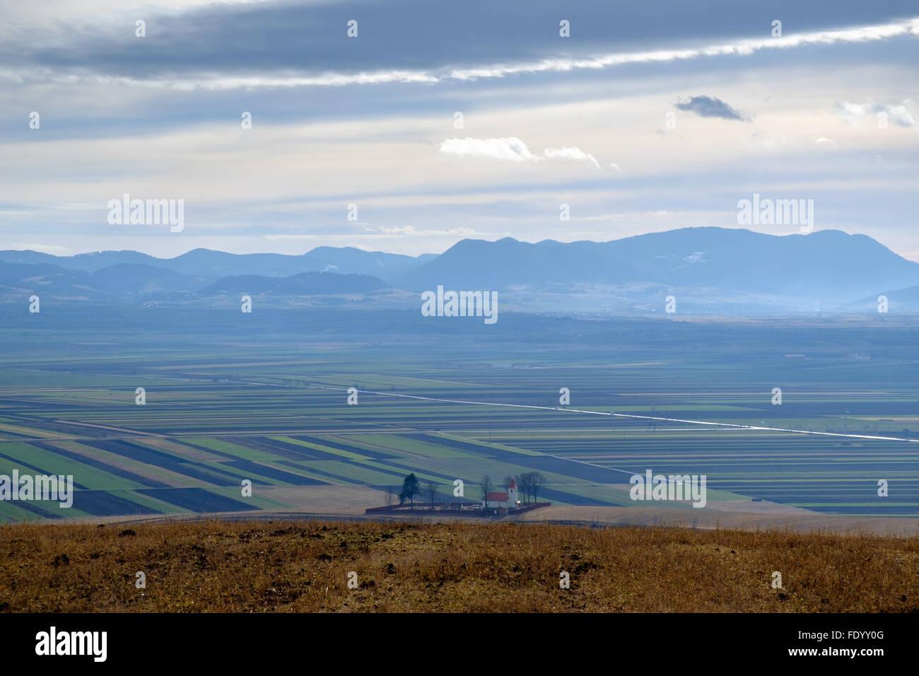 Piccolo villaggio con chiesa cattolica tra le colline e le montagne della Transilvania, la Romania in inverno senza neve Foto Stock