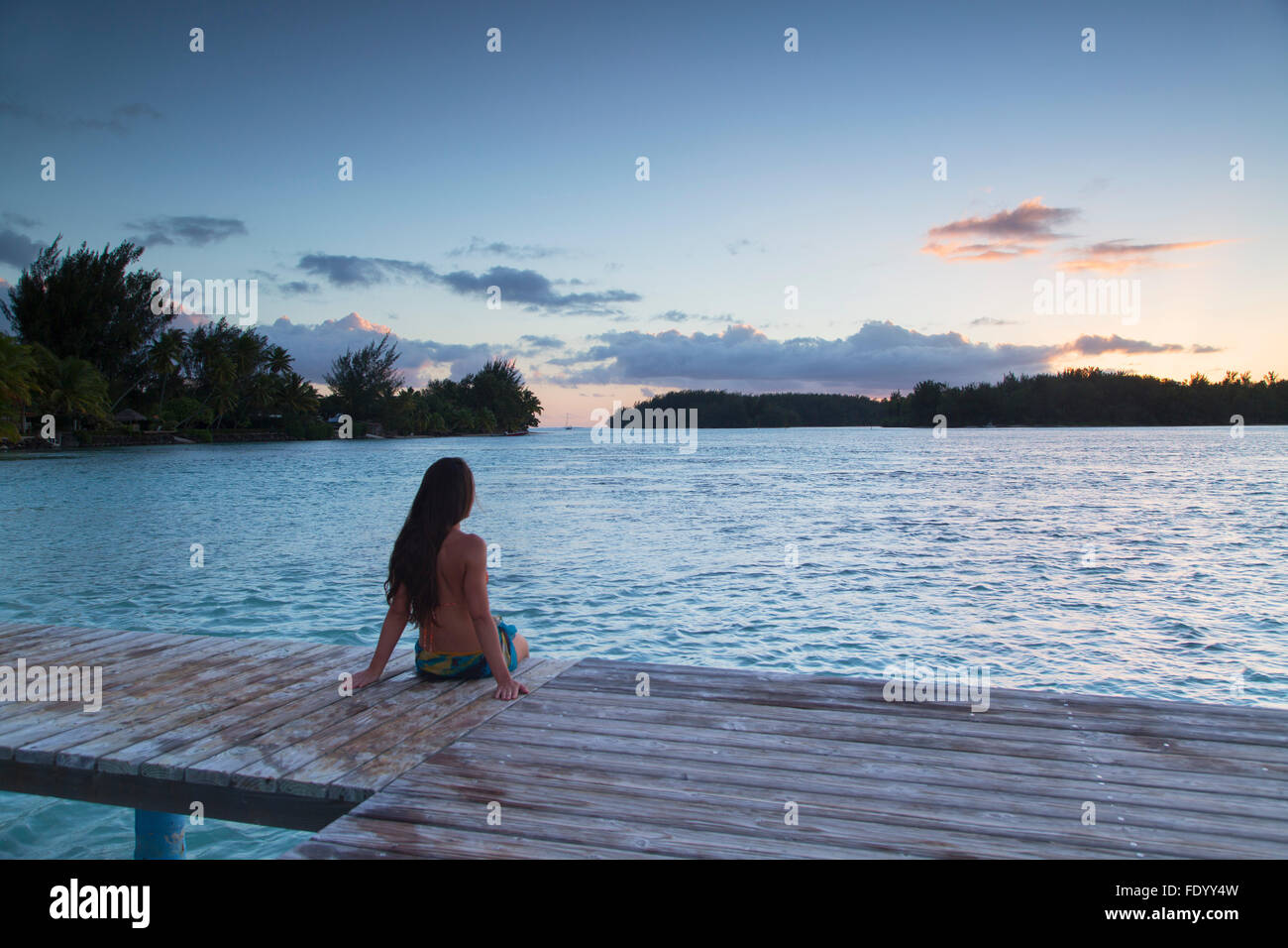 Donna seduta sul molo al tramonto, Hauru Point, Mo'Orea, Isole della Società, Polinesia Francese Foto Stock