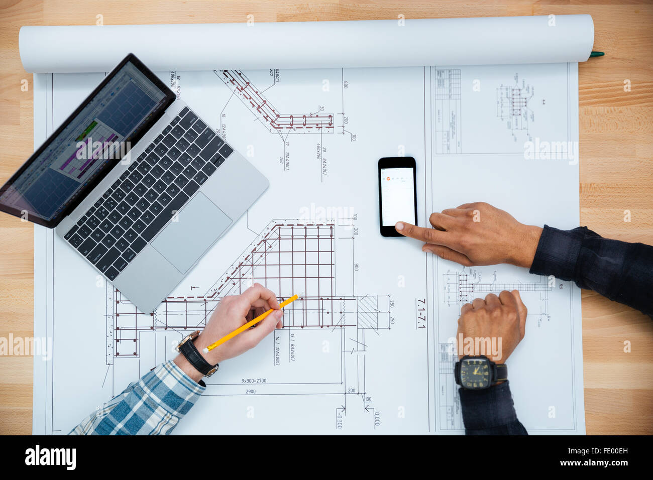 Vista dall'alto di due uomini che lavorano per il blueprint utilizzando il telefono cellulare e il computer portatile Foto Stock