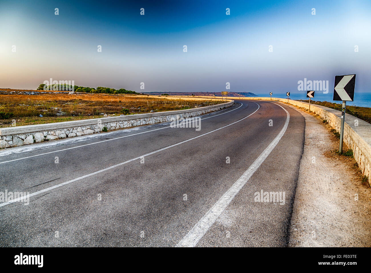 Curva sulla strada asfaltata con asse di mezzeria in Italia, con avvertimento per segnaletica stradale sulla spiaggia Foto Stock