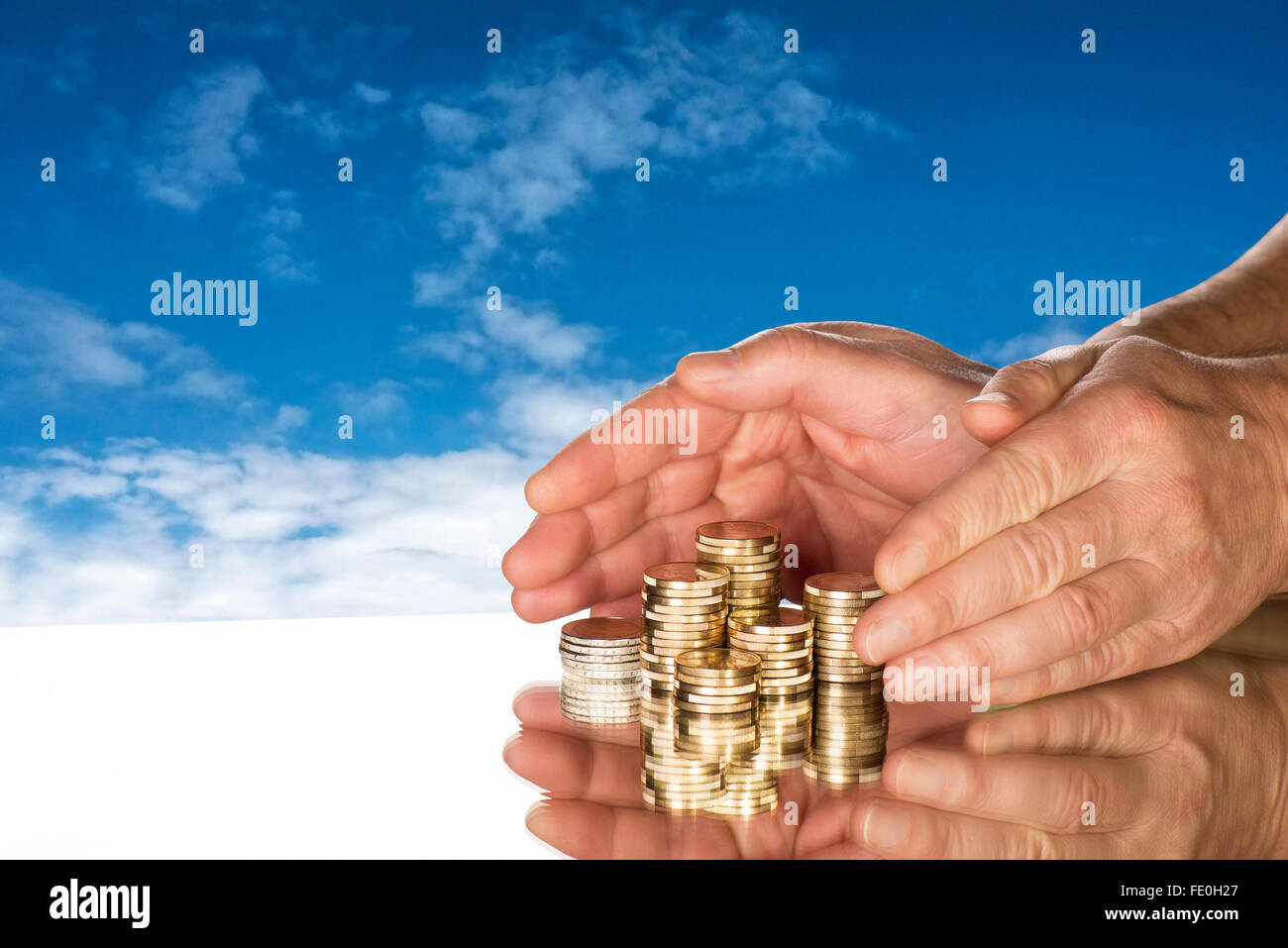 Mani comprendono diverse pile di monete nella parte anteriore del cielo blu. Foto Stock