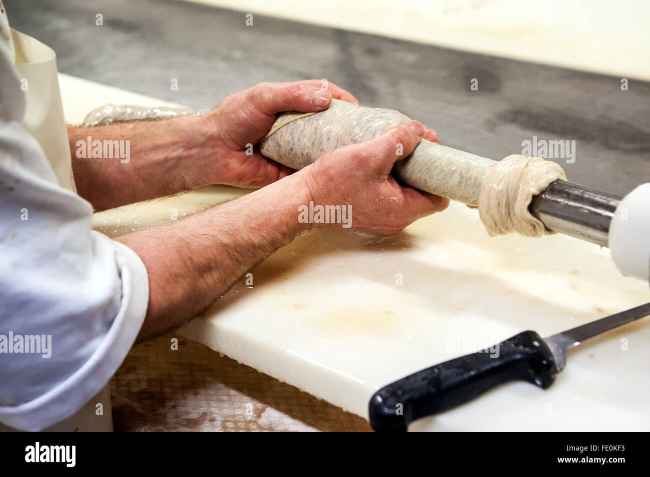 Chiusura del macellaio mani la preparazione di involucro da riempire con il ripieno in un salame impianto di lavorazione Foto Stock