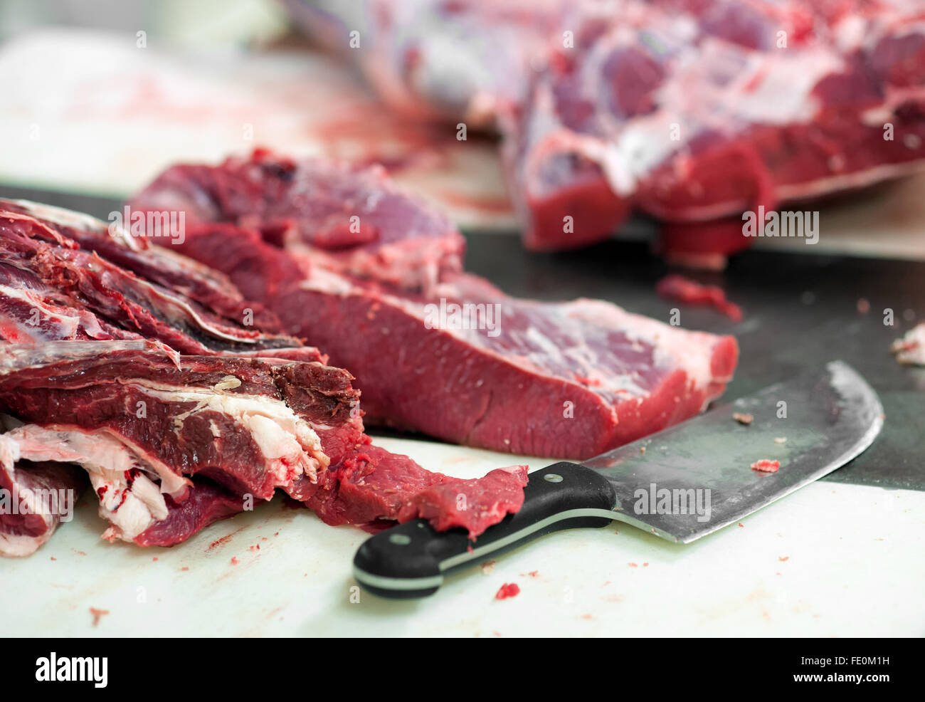 Close up dei tagli di carne cruda sul tavolo affollato con grande coltello in food processing facility Foto Stock