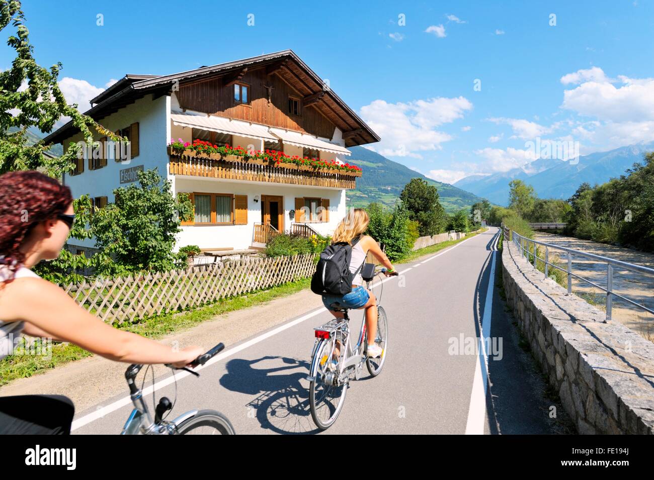 I ciclisti lasciare la medievale città murata di Glorenza in Alto Adige regione dell'Italia. Riverside chalet sulla Via Lungo Adige Foto Stock