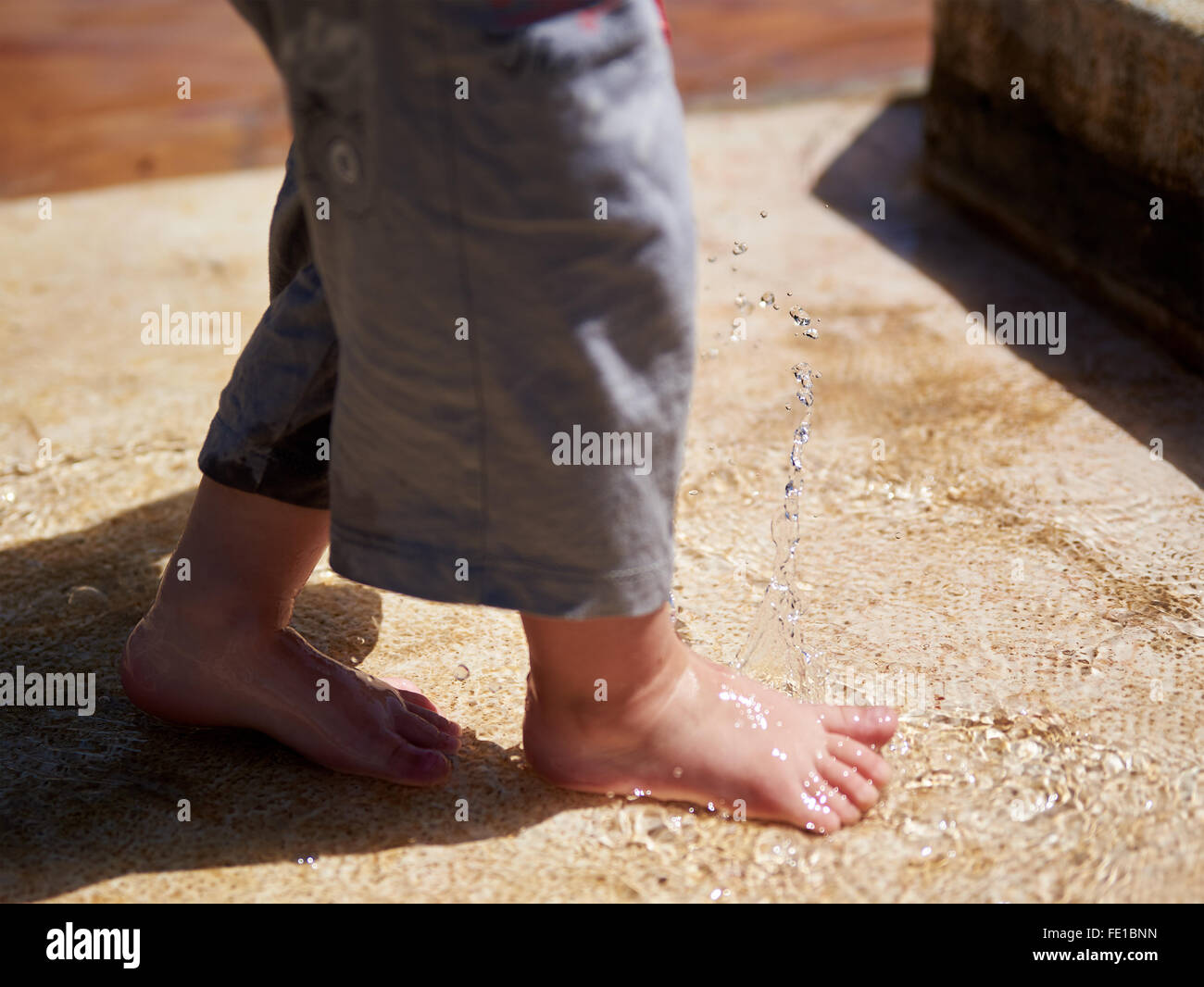 Carino baby boy bambino gioca con acqua e spruzzi spruzzino con piedi Foto Stock